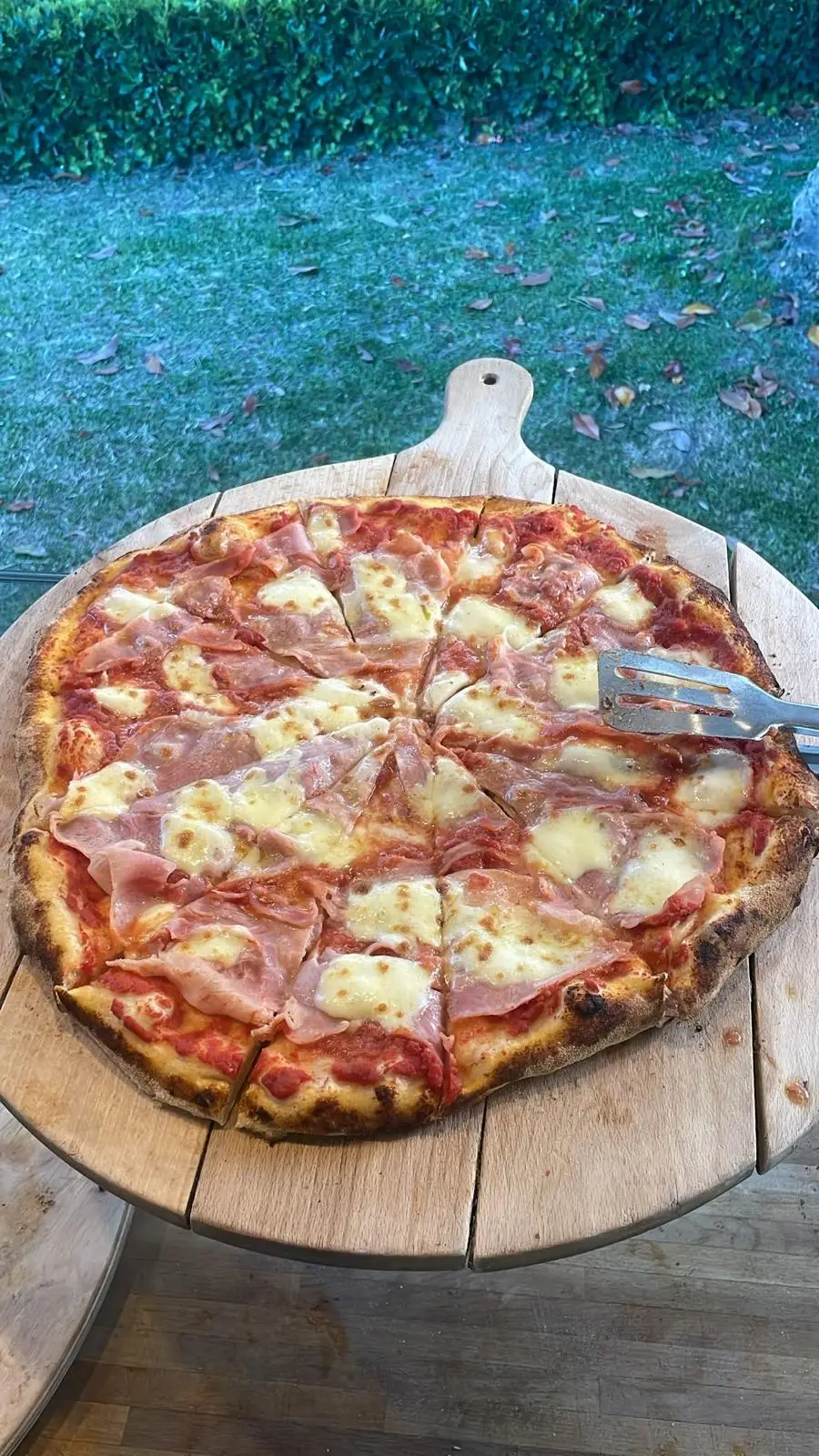 Una pizza al prosciutto sul tagliere di legno, su un tavolo in giardino